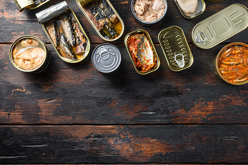 Conserves of canned fish with different types of seafood, opened and closed cans with Saury, mackerel, sprats, sardines, pilchard, squid, tuna,  over  dark wood old table  , top view space for text.