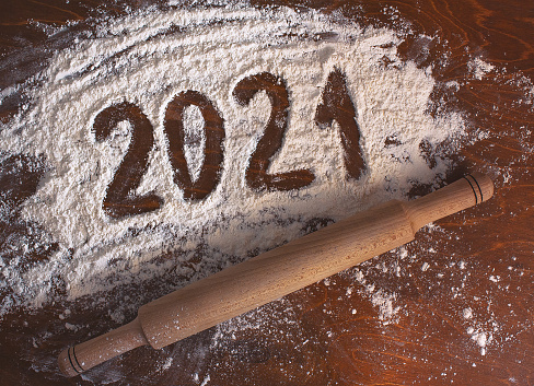the inscription 2021 is handwritten on flour on a wooden table with a rolling pin next to it. new year concept.