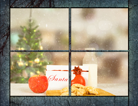 Milk and biscuits for santa on a table view through a window from outside