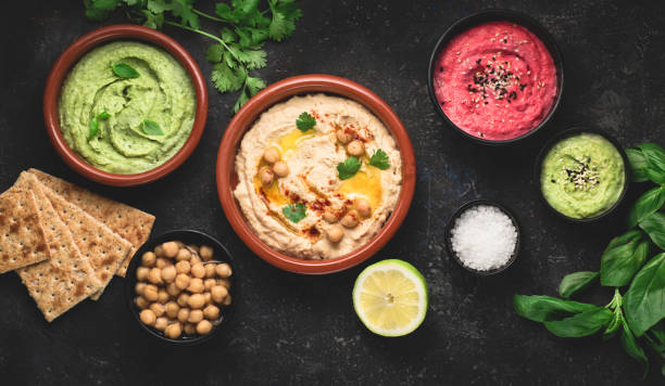 istock Flat lay of various types of vegetarian hummus based on herbs and beets, basil and coriander on a dark rustic background. Healthy food concept 1280119471