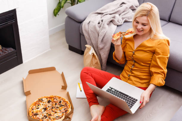 istock Ecommerce woman. Young female using computer for online shopping, sitting on the floor and eating pizza. 1280119867