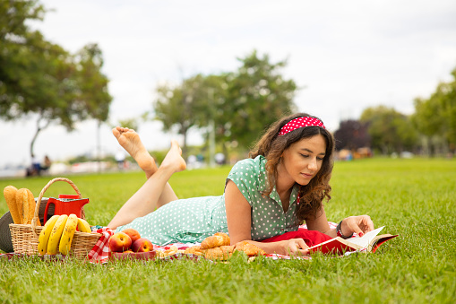 Young woman wearing green dress reading a book while relaxing in the park