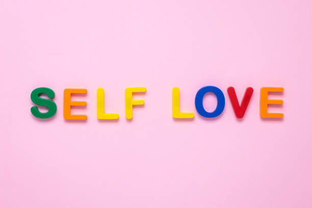 Self love text on pink paper background made from colorful plastic letters. Multicolored inscription on the banner. Title, headline. The psychology concept. The message on the poster, the words. stock photo