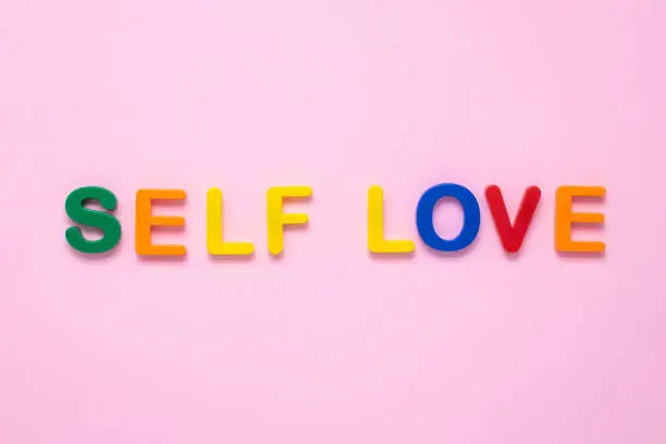 Self love text on pink paper background made from colorful plastic letters. Multicolored inscription on the banner. Title, headline. The psychology concept. The message on the poster, the words