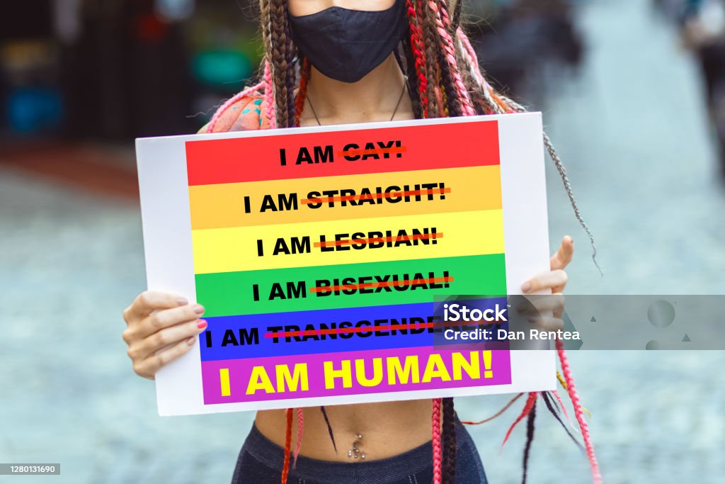 Young lesbian woman activist with face mask protesting against LGBT community discrimination Young woman on street enjoy holding gay pride banner during protest – Mixed race lesbian female wearing mask at pride parade for lgbt rights – Diversity and tolerance for gender identity LGBTQIA People Stock Photo