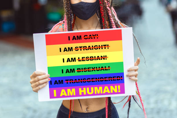 Young lesbian woman activist with face mask protesting against LGBT community discrimination Young woman on street enjoy holding gay pride banner during protest – Mixed race lesbian female wearing mask at pride parade for lgbt rights – Diversity and tolerance for gender identity gay pride parade photos stock pictures, royalty-free photos & images