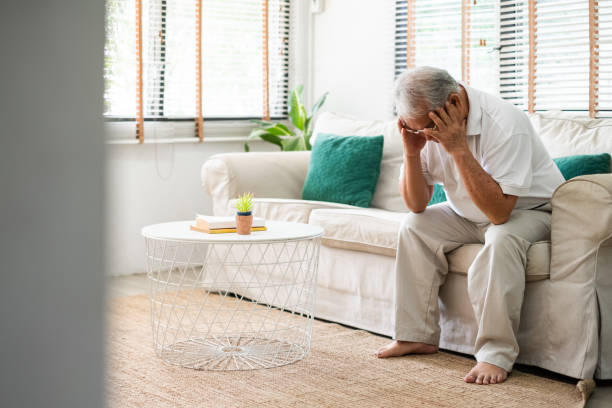 Senior old Asian man feel stressed, headache sitting alone on sofa at home stock photo