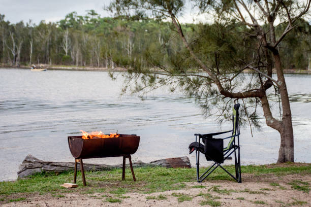 istock Campfire in a half barrel fire pit and empty campchair on the lake. Camping life 1280134683
