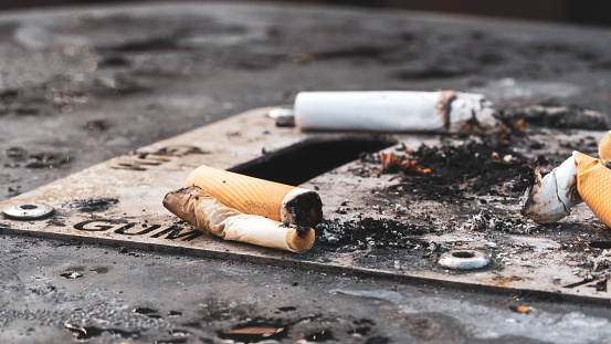 Focus on cigarette butts on an outdoor ashtray bin