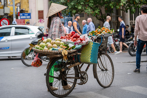 Hanoi, Vietnam - march 01, 2020 : Vietnamese woman with bike selling tropical fruit on the street food market of old town in Hanoi, Vietnam