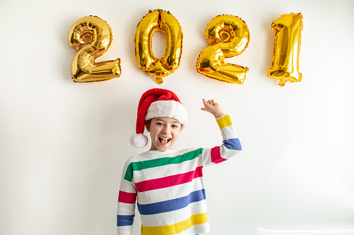 Little cute girl wearing a Santa hat, she is standing in front of white wall and pointing