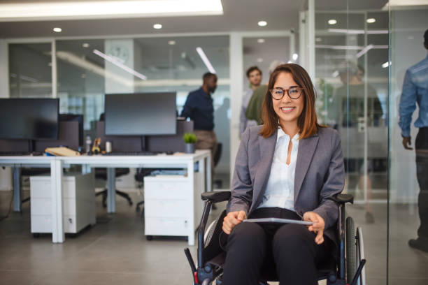 Disabled business woman in wheelchair holding table smiling in office Disabled asian business woman in wheelchair holding digital tablet and looking at camera smiling in modern office physical disability photos stock pictures, royalty-free photos & images