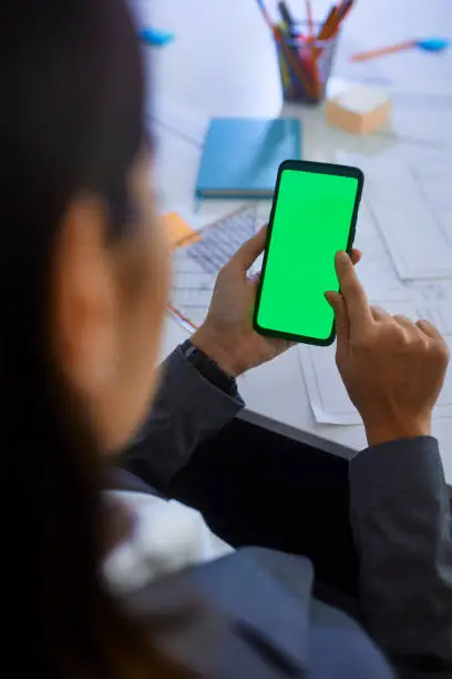 Close-up of business woman swiping through mobile phone green screen at her office