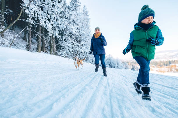 mutter und sohn haben spaß. sie laufen mit ihrem beagle-hund im verschneiten wald beim hundespaziergang. mutter und sohn verwandte und femily werte konzeptbild. - snow dog walking running stock-fotos und bilder