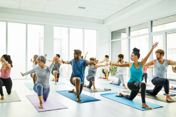 Never underestimate the power of yoga Shot of a group of men and women practicing yoga in a fitness class warrior 2 stock pictures, royalty-free photos & images