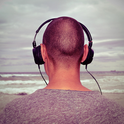 closeup of a young man seen from behind listening to music with headphones in front of the sea