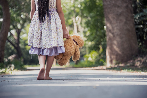 Sad girl hugging teddy bear sadness alone in green garden park. Lonely girl feeling sad unhappy walking outdoors with best friend toy. Autism child play teddy bear best friend. Family violence concept