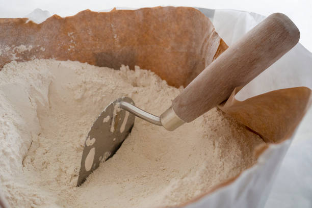 Close-up of plaster trowel in full open paper bag of putty powder for wall decoration,caulk or glaze.Concept of building materials.Finish coating in dry cement powder form.Selective focus,copy space primer plano de la paleta de yeso en bolsa de papel abierto completo de polvo de masilla para la decoración de la pared, calafateo o esmalte. concepto de materiales de construcción. recubrimiento de acabado en polvo de cemento seco. enfoque selectivo, es