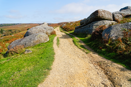 Rugged path runs between gritstone  gently up hill between gritstone boulders on an autumn morning in Derbyshire