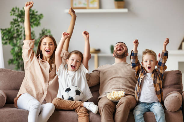 family of fans watching a football match and celebrating goal on TV at home A family of fans mother father and children watching a football match and celebrating goal on TV at home excited football fan cheering for his team on tv stock pictures, royalty-free photos & images