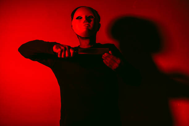 istock Man in white Halloween mask with butcher knife making slaughter gesture with red light 1280157413