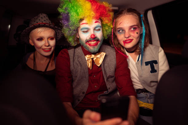 Friends in costumes, driving in the car on Halloween night while a young man is using his phone Friends in costumes, driving in the car on Halloween night while a young man is using his phone. period costume stock pictures, royalty-free photos & images