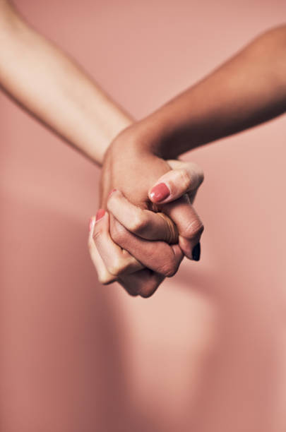 Shot of two unrecognizable women holding hands against a pink background
