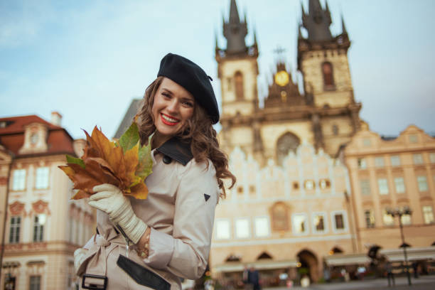 femme moderne de sourire dans le trench-coat beige et le béret noir - hôtel de ville de prague photos et images de collection