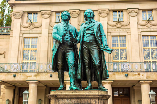 Weimar, Germany - December 23, 2014: The Statues of Goethe and Schiller Located in Weimar.\n\nThe statues of Johann Wolfgang von Goethe and Friedrich Schiller, located in Weimar, Germany, are iconic monuments paying tribute to two of the country's most renowned literary figures. Positioned in front of the German National Theatre in Theaterplatz, the statues symbolize the enduring friendship and intellectual collaboration between Goethe and Schiller, who were pivotal figures in German literature during the Classical and Weimar Classicism periods.\n\nThe statues were unveiled in 1857 and sculpted by Ernst Rietschel. The monument features Goethe and Schiller in animated conversation, embodying the spirit of intellectual exchange and artistic collaboration that defined their relationship. The site has become a symbol of Weimar's cultural heritage, attracting visitors and literature enthusiasts from around the world. It stands as a fitting tribute to the profound impact Goethe and Schiller had on German literature and intellectual thought during a pivotal era in the country's cultural history.