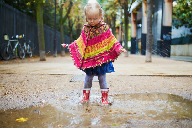 istock Child wearing red rain boots and jumping in puddle on a fall day 1280168719