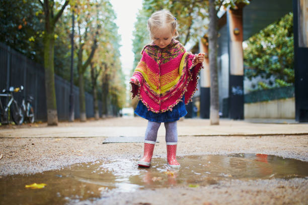 istock Child wearing red rain boots and jumping in puddle on a fall day 1280168775