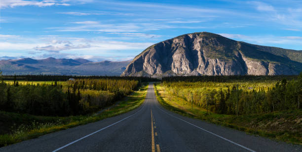 Scenic Route, Alaska Hwy, during a sunny and cloudy sunset. Scenic Route, Alaska Hwy, during a sunny and cloudy day. Mountains in Background. Near Haines Junction, West of Whitehorse, Yukon, Canada. middle of the road stock pictures, royalty-free photos & images