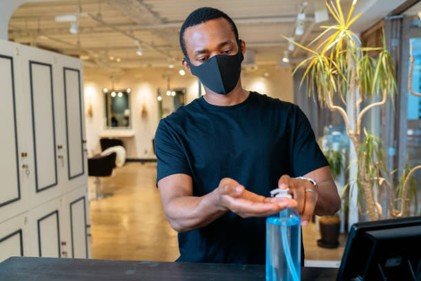 Man disinfecting his hands at barber shop A man is disinfecting his hands at the entrance of a barber shop. black barber stock pictures, royalty-free photos & images