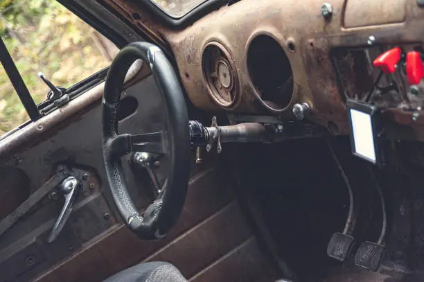 Interior of an old truck. Rusted dashboard with missing items and steering wheel. Modern LCD screen visible.