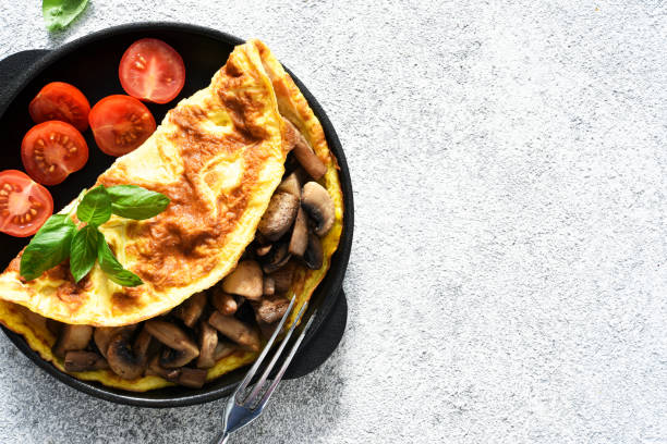 istock Omelet with mushrooms and tomatoes for breakfast with orange sticks on a white concrete background. 1280171074