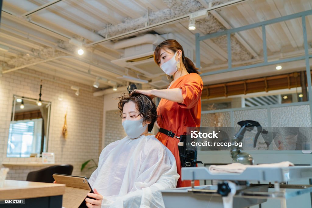 Haar-Dresser trocknen Kunden Haare. Besitzer und Kunde tragen Schutzmaske zur Krankheitsprävention - Lizenzfrei Friseursalon Stock-Foto