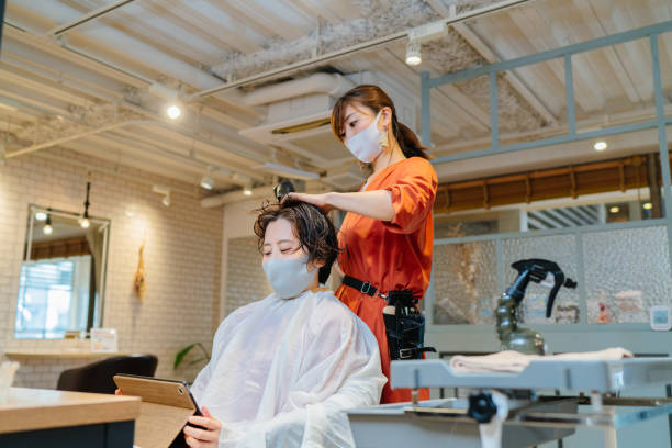 cabeleireiro secando o cabelo do cliente. proprietário e cliente usando máscara facial protetora para prevenção de doenças - for - fotografias e filmes do acervo