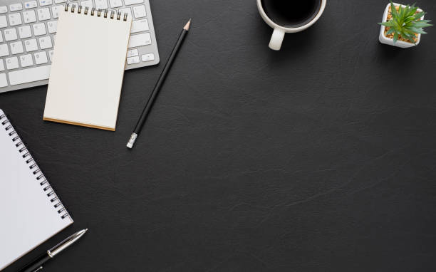 istock Top view above of Black leather office desk table with keyboard, notebook and coffee cup with equipment office supplies. Business and finance concept. Workplace, Flat lay with blank copy space. 1280171879