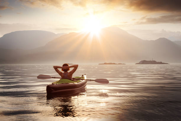 mulher relaxando em seu caiaque durante um pôr do sol de verão colorido. - golden sunset - fotografias e filmes do acervo