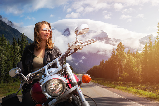 Caucasian Biker Woman on a Motorcycle on a scenic Road in the Canadian Rockies. Image Composite. Background from British Columbia, Canada.