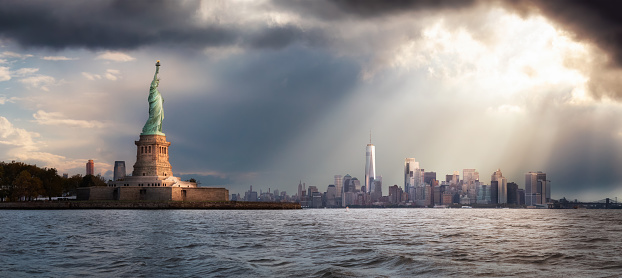 Panoramic view of the Statue of Liberty and Downtown Manhattan in the background during a vibrant cloudy sunrise. Taken in New York City, NY, United States.