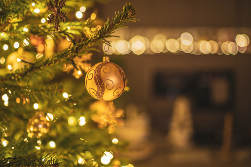 beautiful golden decorated christmas tree bauble on illuminated fir tree in house in the evening, shallow focus, background blurred, place for text