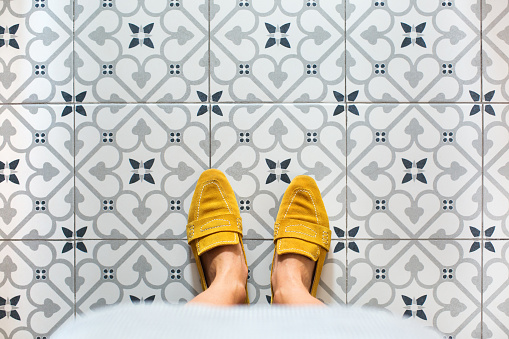 Female legs, feet in yellow shoes on a mosaic tile floor. Top view, flat lay selfie on a vintage seamless background, copy space\