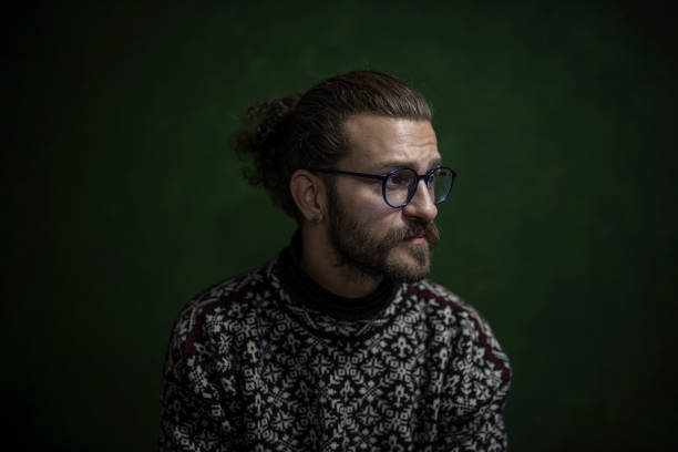 Portrait of a man in sweater, with eyeglasses, with a beard on dark background.