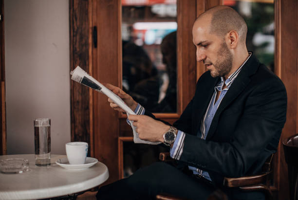 istock Handsome young businessman reading newspaper in sidewalk cafe 1280184170