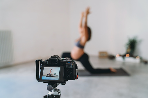 Yoga teacher is recording a pregnancy yoga lesson to upload it online. She's preparing an online yoga class.