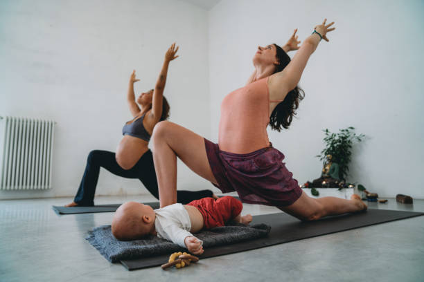 two friends practicing yoga together, one of them is pregnant and the other one has a little child - relaxation exercise child mother human pregnancy imagens e fotografias de stock