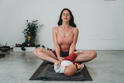 A young mother practicing yoga with her little child. Caucasian ethnicity.