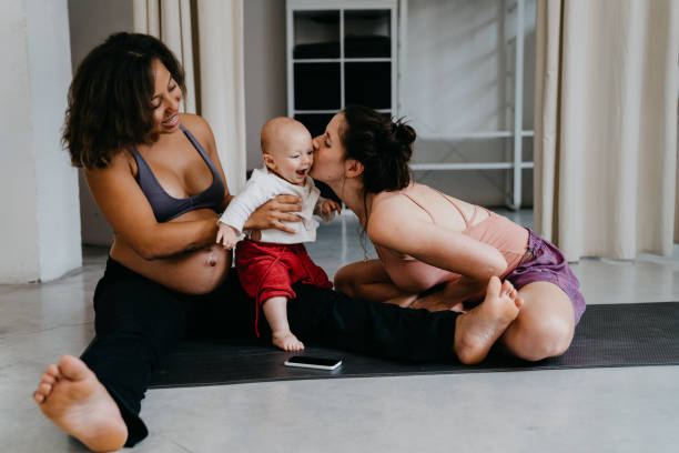 Two young women playing with their son in a yoga studio Two young women playing with their son in a yoga studio. They are sitting on the floor on a yoga mat. 3 months pregnant belly stock pictures, royalty-free photos & images