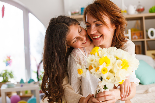 Shot of affectionate teenage girl embracing her mother and giving her a beautiful bouquet of daffodils as a gift for Mother's day.